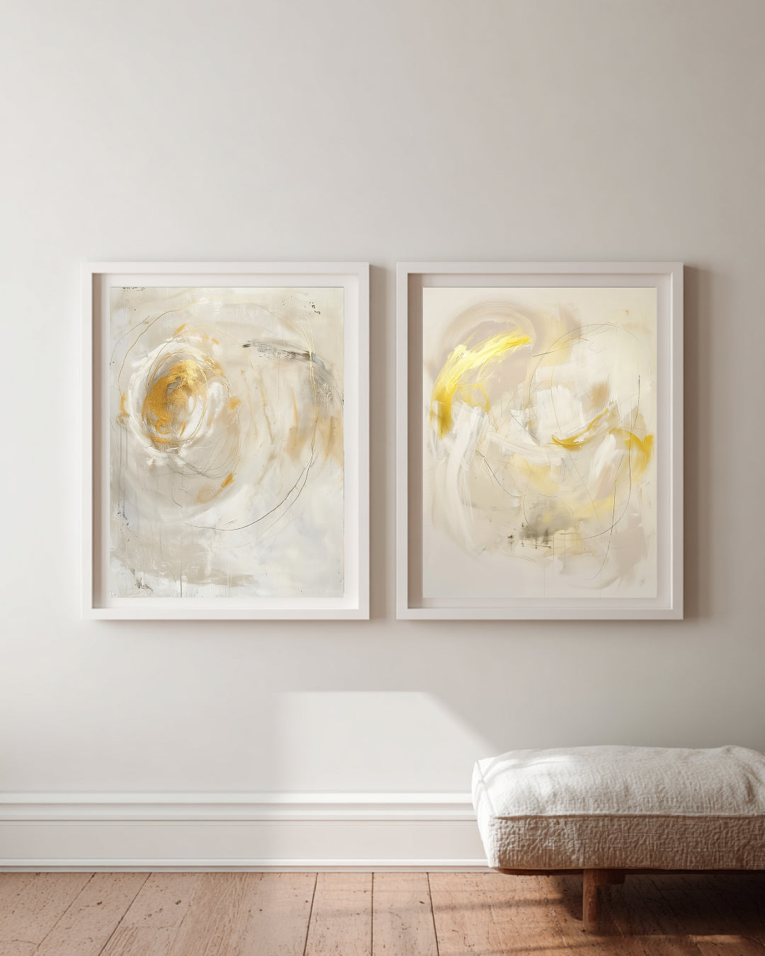 Two abstract art pieces in white frames on a wall with a wooden floor and cushioned bench.