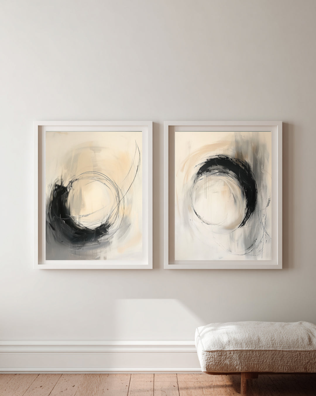 Two abstract art pieces in neutral tones on a wall with a wooden floor and white bench.
