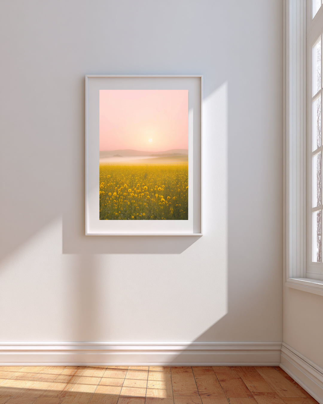 Framed artwork of a yellow field with a pink sky on a white wall.